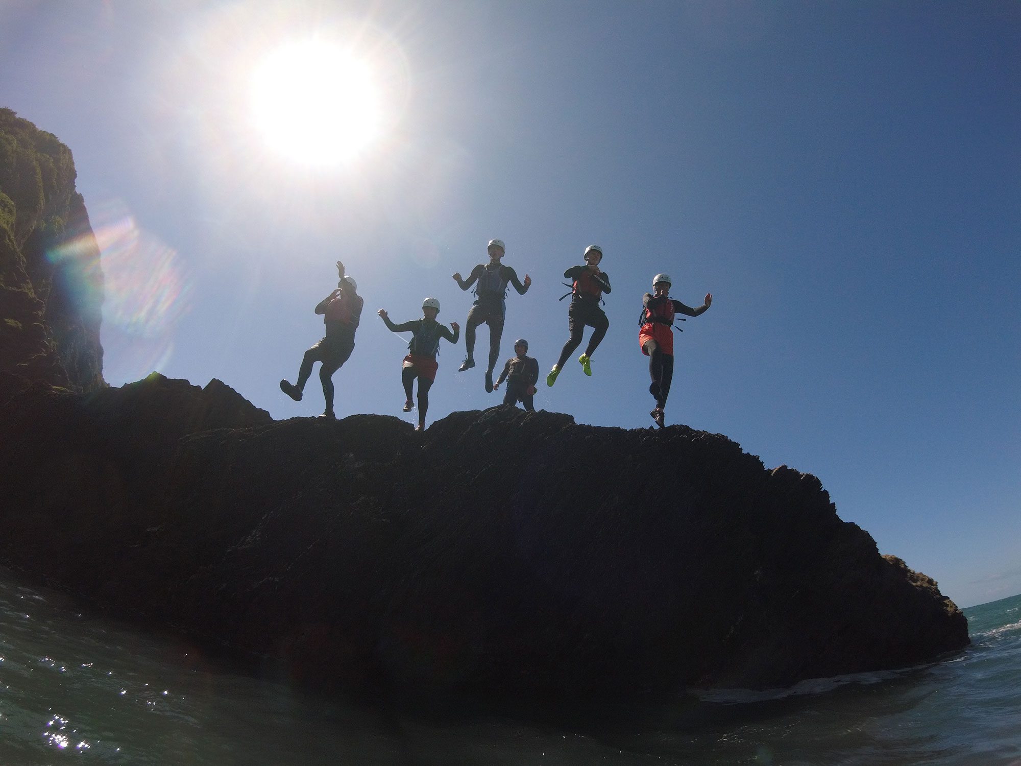 A group of people coasteering jump off a cliff on a corporate away day in North Devon