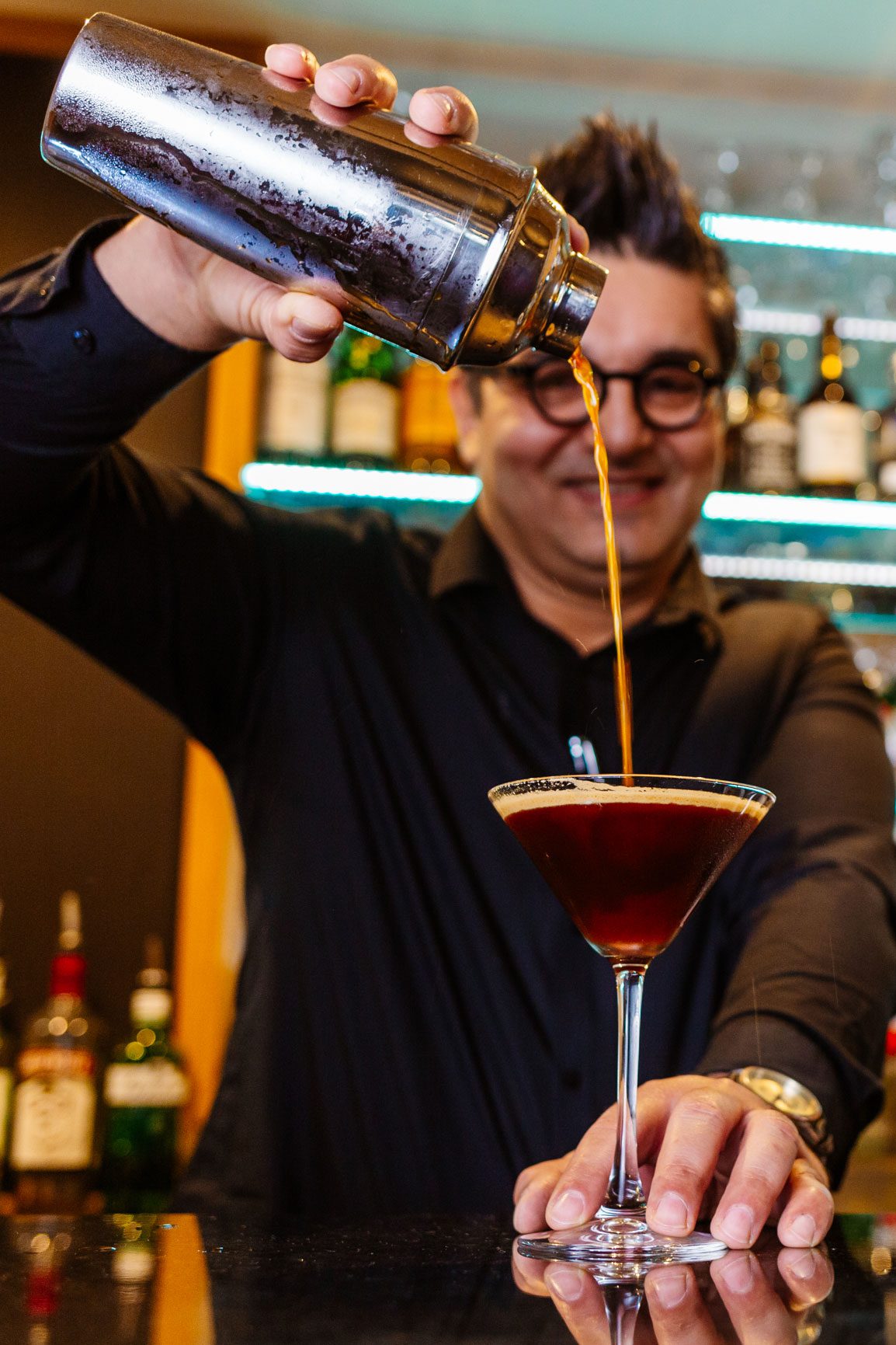 A middle age man dressed in black pours an espresso martini cocktail into a cocktail glass at the bar of The Carlton Hotel in Ilfracombe