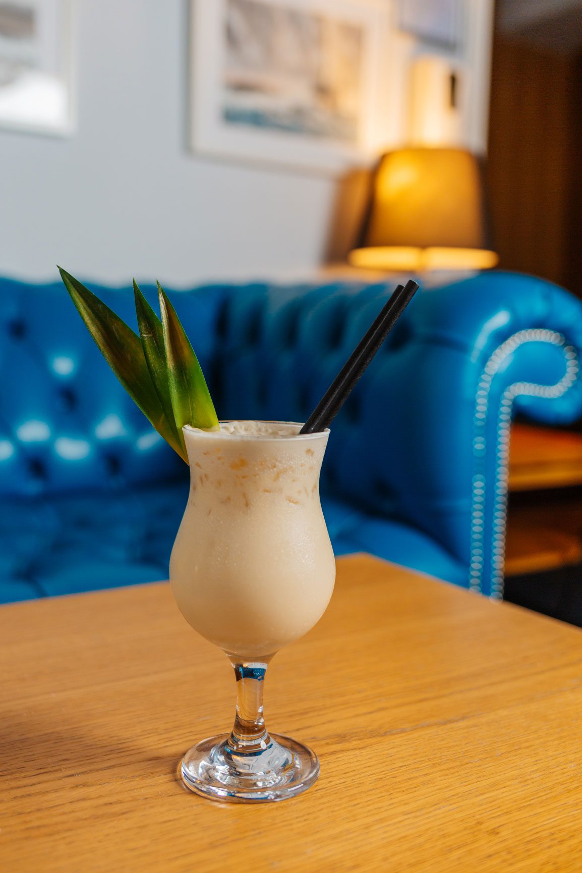 A Pina Colada cocktail on a table with a blue sofa behind